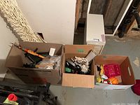 Boxes filled with assorted items including toys, games, wooden duck decoys, fishing rods, and office supplies against basement wall