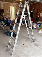 Full view of 6 ft aluminum step ladder standing open in garage, showing structure and steps.