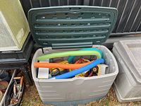 Open Rubbermaid deck box with pool noodles and toy trucks inside.