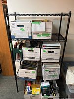 Front view of four-tier black metal wire shelving unit with boxed contents stored on shelves