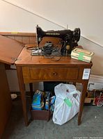 Vintage Singer sewing machine set on wooden sewing table with sewing accessories beneath and electrical cord on top.