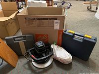 Wide shot of all tools including Wen Orbital Car Waxer, two carrying cases, tool belt, and bagged item on gray carpet.