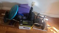 Wide view of exercise equipment including dumbbells, yoga blocks, ankle and wrist weights box, and balance disc.