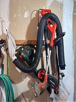 Black & Decker Vac'n'Mulch blower hanging with flexible hose and collection bag, showing blower body and hose attachments
