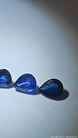 Three pear cut deep blue sapphires shown lying flat on a white surface, highlighting rich color and cut.