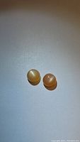 Two peach moonstones with cat's eye effect placed on a white background, showing glossy, domed cabochon cut surface and luminous bands