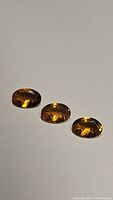 Three oval cut Fanta orange tourmaline gemstones displayed on white background showing facets and color