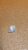 Pear-shaped opal gemstone with intense rainbow colors on a textured brown surface.