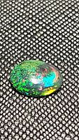 Close-up image of oval Ethiopian black opal with green, blue, red, and yellow color flashes on textured black background.