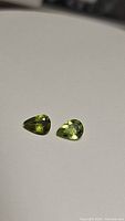 Pair of natural pear-shaped apple green peridot gemstones shown on neutral background, highlighting color and cut.