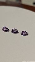 Three pear-shaped natural amethyst gemstones displayed on a white background showing their shape, size, and color.