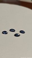 Four marquis cut cornflower blue sapphires arranged on a beige surface, showing size and shape details.