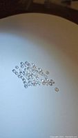 Cluster of small diamond cut white topaz gemstones on a white surface, showing size and clarity.