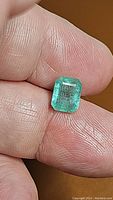 Top view of loose emerald held between fingertips
