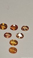 Seven oval cut natural African sapphires in orange to peach shades arranged on pale surface