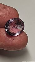 Close-up of a natural purple amethyst gemstone showing the oval checkerboard cut and clarity, held between fingers.