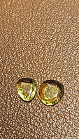 Two natural yellow free form cut sapphire gemstones placed on textured brown surface, showing color and condition