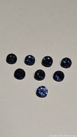 Seven round cut gemstones in dark royal blue and medium cornflower blue colors arranged in a group on a grey background.