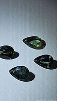 Four natural pear cut green sapphires on white background displaying bright multicolored green colors and good clarity.