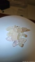 Photo shows a group of 15 natural raw morganite crystals with peach and light pink hues laid on a white surface with a shadow cast to the side.