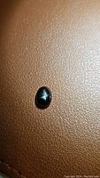 Natural untreated black star diopside oval cabochon on textured brown surface under diffuse light.