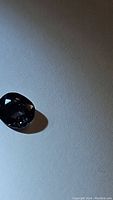 Photo showing an oval sapphire with dark blue to purple hues resting on a light surface with shadow.