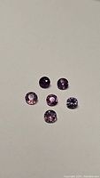Six round faceted sapphires in varying shades of pink and purple displayed on a neutral background.