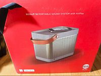 Photo of original Bang & Olufsen Beolit 12 red packaging box with image of the speaker and AirPlay branding.