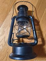 Front view of black metal oil lamp showing glass globe and wire handle