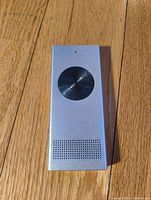 Front view of the silver Enence handheld personal translator with circular black control pad and speaker grille.