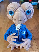 Front view of E.T. plush doll showing detailed facial features and blue hoodie with logo.