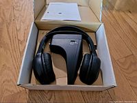 Black wireless headphones with cushioned ear pads resting inside box along with instruction manual.