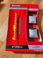 Opened original box showing two Hotronic footwarmer heating units in red packaging with visible wear on box.