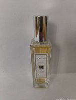 Front view of a almost full Jo Malone London Cologne bottle with silver cap on plain background.