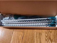 Five clear cylindrical LED light tubes with clear bulbs inside, green end caps, and green cords packed in a cardboard box.