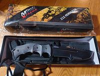 MTech Xtreme branded box and knife in sheath on hardwood floor, showing packaging and knife overall.
