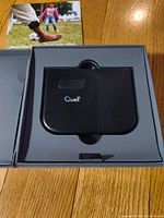 Closed box showing the Quell pain relief device inside molded plastic compartment on wooden floor.