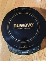 Top view of black Nuwave induction cooktop showing brand logo and circular cooking surface with gold accents