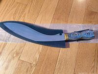 Full view of kurki tool in sheath, showing curved blade and handle detail.