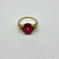 Front view of the 10k yellow gold ring with a round red gemstone and floral side accents.