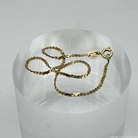 Yellow gold thin chain bracelet displayed on a white cylindrical stand, showing full length and clasp.