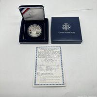 Photo of coin and certificate displayed together; coin inside blue velvet case with US Mint logo