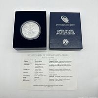 Photo showing the 2015 American Eagle silver coin in a protective case inside its original blue presentation box, along with the specifications sheet.