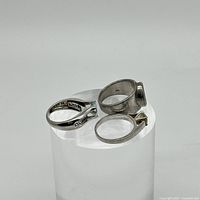 Three silver rings shown from an angled top view revealing their design details and shape.