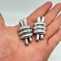 Hand-held view showing size and puffy knot design of vintage silver clip earrings.