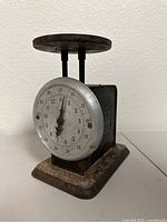 Front view of the antique Pelouze Standard scale showing the round dial with measurement numbers and the top weighing platform.