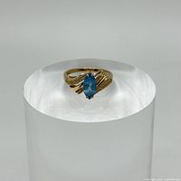 Front view of 14k gold bypass ring with marquis shape blue center stone on display stand.