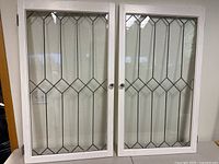 Full view of the pair of white framed windows with diamond pattern leaded glass panes.