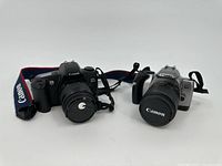 Two Canon EOS Rebel DSLR cameras displayed side by side, showing front views with lens caps on and attached Canon straps.