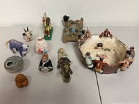 Overview photo of the lot containing small clay and wood figural sculptures including animals and people, and a ceramic flower frog bowl with figures on the rim.